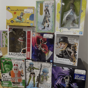 Row of boxed anime figure collectibles stacked on a light surface against a white wall, ready for display.