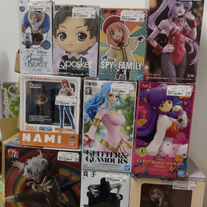 Stack of colorful anime figure boxes arranged in a display, including SPY×FAMILY, Qposket, and Glitters & Glamours lines with price stickers visible.