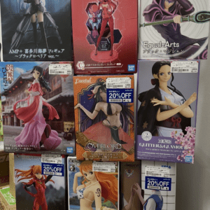 Assorted anime figure boxes stacked on a wall display, featuring colorful character art from various series and brands like Bandai and Konami.