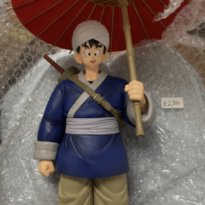 Toy figure of a character in a blue tunic and tan pants, wearing a white head wrap and holding a red umbrella, standing among bubble wrap.