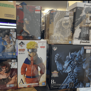 Boxed anime figures on a store shelf, including Naruto Uzumaki center, Street Fighter characters bottom left, and other figures around.