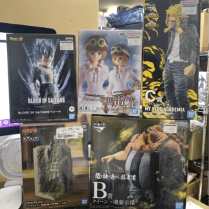 Assorted anime figure boxes on a store shelf, including Blood of Saiyans, One Piece Koala, My Hero Academia, and Naruto statues/figures on display