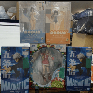 Display of several anime figure boxes on a store shelf, including two Pop Up Parade boxes on the top row (blue and orange) and blue MaxiMatic boxes at the bottom, with other boxed figures in between to the sides.