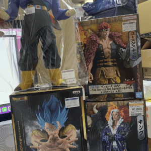 Large Dragon Ball Z action figure in a purple jacket with yellow boots, wrapped in plastic, standing on display boxes in a store.