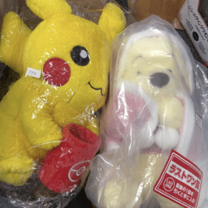 Two plush toys in plastic bags: a yellow Pikachu with red cheeks on the left and a pale bunny-like character on the right.
