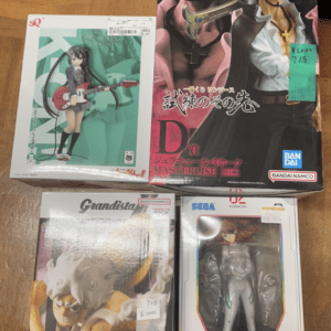 Group of boxed anime figures laid on a wooden floor, including a large One Piece Masterlise box with two pirates and three smaller figure boxes nearby.