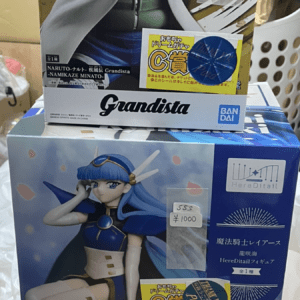 Stacked anime figure boxes: Naruto Grandista top, blue-haired heroine middle, pink-clad character bottom, with price stickers visible on boxes.
