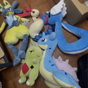 Pile of colorful plush toy dragons and creatures on a wooden floor, appearing soft and cuddly.