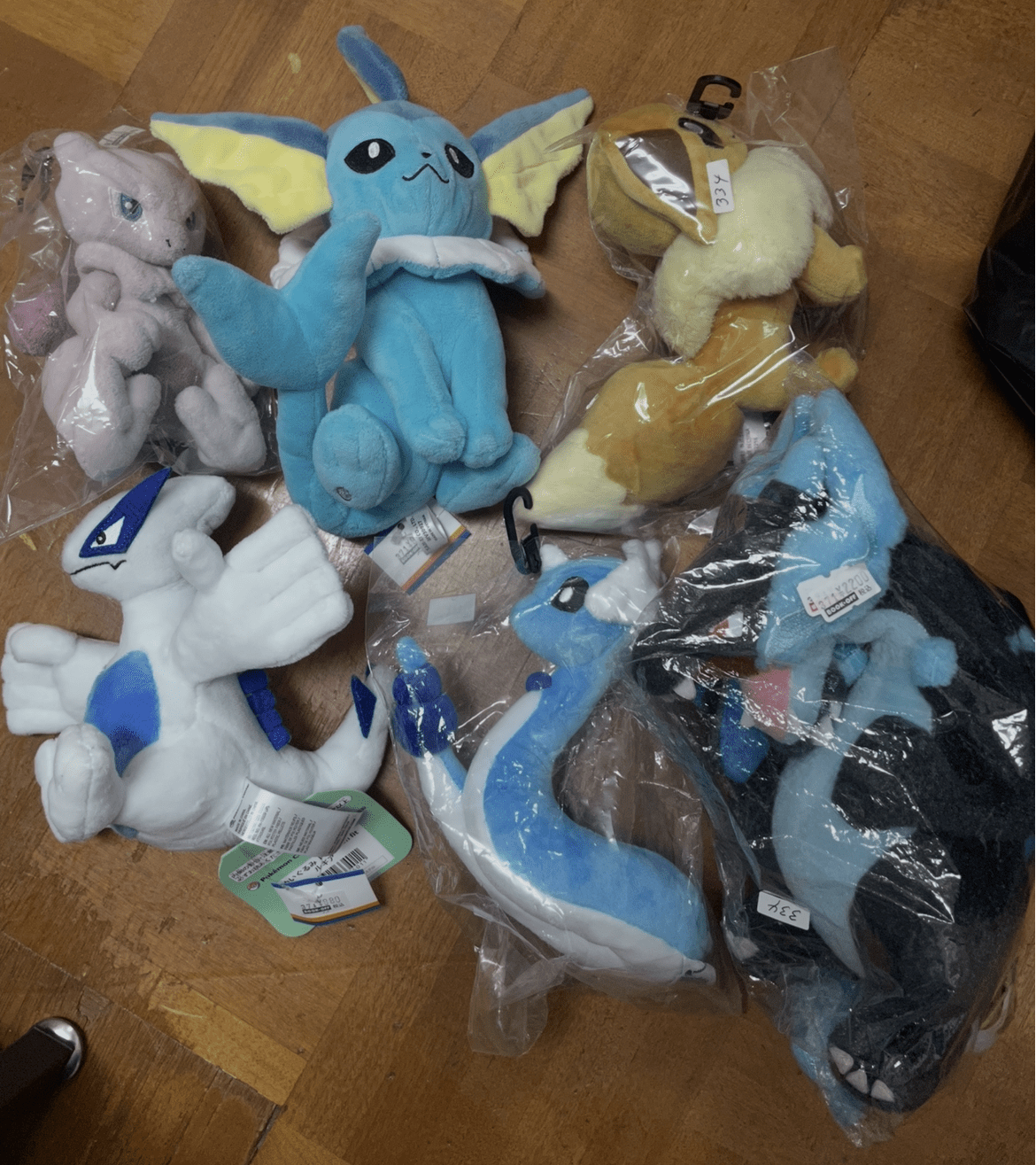 Ver Fotos Recientes 227 - Articulos Japan (post Box Japan) Assorted plush toy Pokémon and fantasy characters in plastic bags on a wooden floor. Articulos Japan (Post Box Japan)