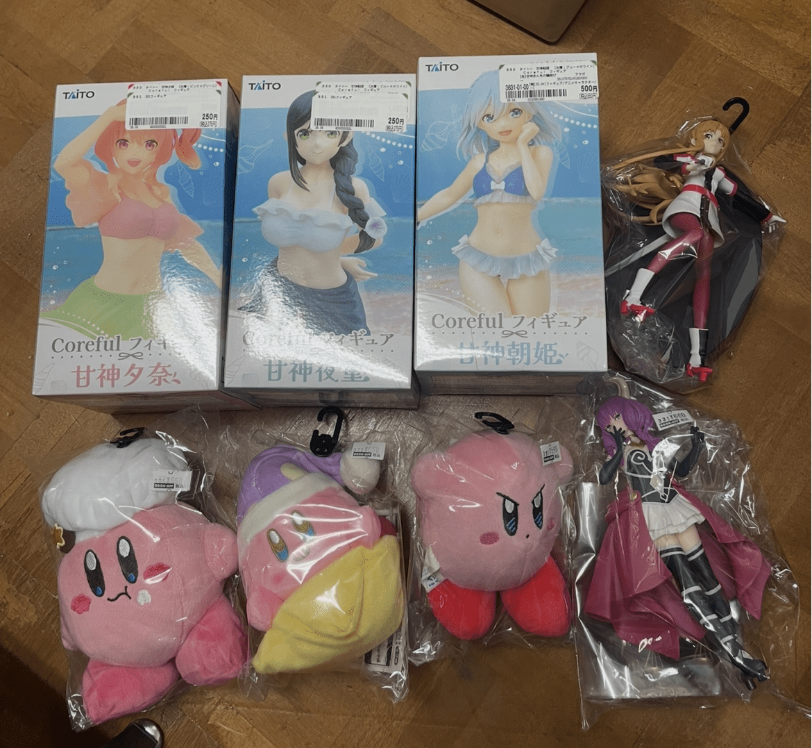 Ver Fotos Recientes 228 - Articulos Japan (post Box Japan) Three Coreful anime figure boxes showing beachwear characters, with an unboxed figure in plastic and three pink Kirby-style plush toys on a wooden floor. Articulos Japan (Post Box Japan)