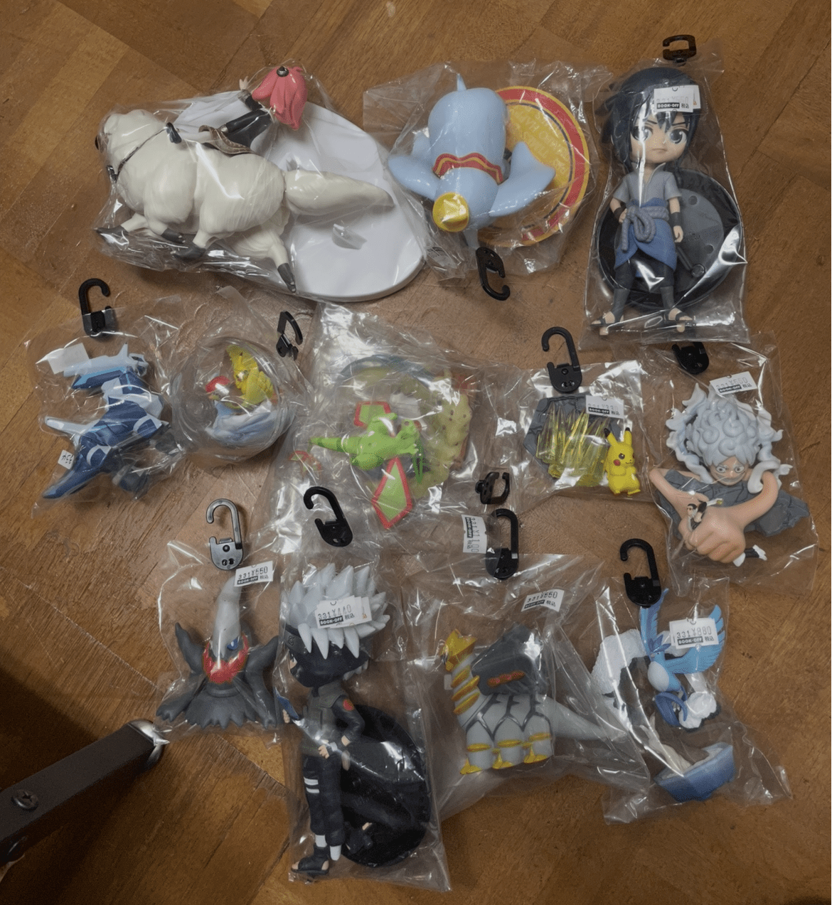 Ver Fotos Recientes 229 - Articulos Japan (post Box Japan) Several anime figurines sealed in plastic bags laid out on a wooden floor, showing a variety of characters and poses (including a blue rabbit-like figure and a blue-haired character). Articulos Japan (Post Box Japan)