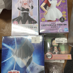 Collection of anime figure boxes on a wooden table: two tall boxed characters on top, one blue box featuring a Yu-Gi-Oh character on the bottom left, and a small figure in plastic packaging on the bottom right