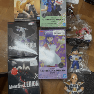 Assorted boxed anime figures laid on a wooden floor, including a blue-haired character box and several others with price stickers.