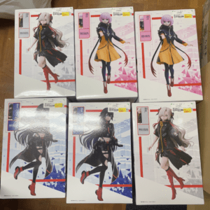 Boxed anime figure packages showing female characters in dynamic poses, arranged in two rows on a wooden floor.