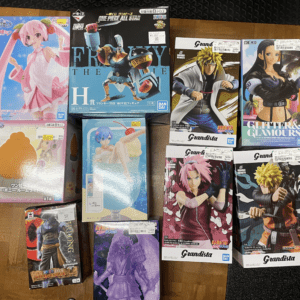 A top-down view of multiple anime action figure boxes arranged on a wooden floor, featuring characters from Naruto, One Piece, and other series with colorful packaging.