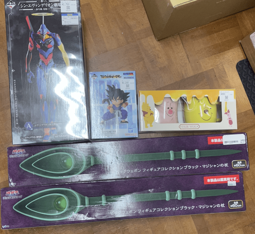 Ver Fotos Recientes 256 - Articulos Japan (post Box Japan) Collection of anime figures and themed goodies on a wooden floor: Evangelion figure box, Dragon Ball mini figure box, Pooh/Mickey mug set, and two long green weapons boxed for display Articulos Japan (Post Box Japan)