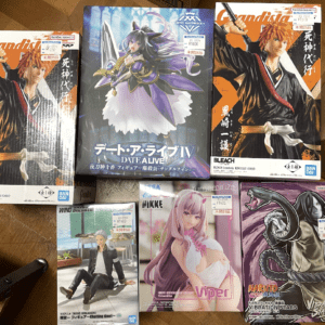 Five anime figure boxes on a wooden table: Fecha A Live IV figure in the center, Bleach Kurosaki Ichigo boxes on left and right, plus a Naruto Vibrational Stars box and a pink-haired Viper figure box at the bottom.