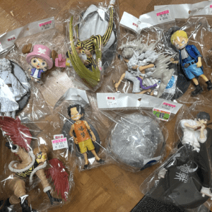 Collection of anime action figures in plastic bags laid out on a wooden floor, various poses and outfits visible.