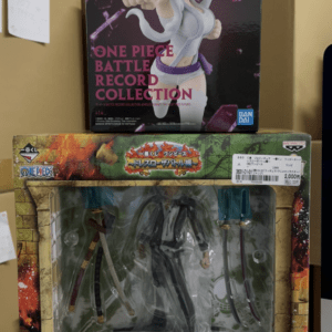 Stack of boxed anime figures on a shelf: the top box shows a One Piece Battle Record Collection figure with white-haired character in a dynamic punching pose. The lower box contains a transparent window displaying another figure with swords inside.