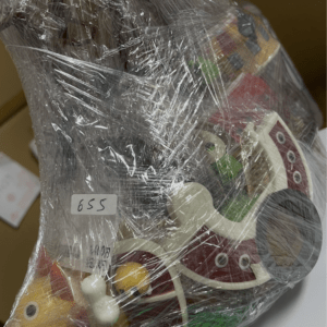 Wrapped gift basket with colorful wooden toy shapes visible through clear plastic wrap, ready for gifting.