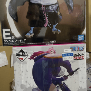 Two stacked Bandai Namco One Piece prize boxes on a shelf; top box shows a large blue-skinned character with a white shirt and black belt, bottom box features a dynamic pink-haired female figure in a purple outfit with a weapon. Both boxes display E prize markings and One Piece branding.  Articulos Japan (Post Box Japan)