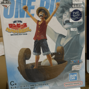 One Piece Monkey D. Luffy figure standing on a wooden raft with arms raised on a product box with large blue 'ONE PIECE' text behind him.