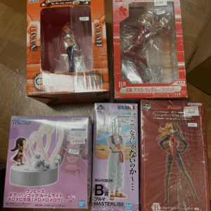 Several boxed anime figures arranged on a wooden floor, price stickers visible on boxes (One Piece and other series).