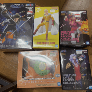 Boxed anime figures on a wooden floor, including One Piece and One Punch Man collectibles. Intended as display boxes for action figures.