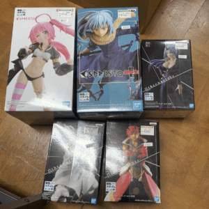 Five boxed anime figures on a wooden floor: pink-haired fighter, blue-haired cloaked warrior, purple-haired woman, and two more figures in darker boxes (Otherworlder).