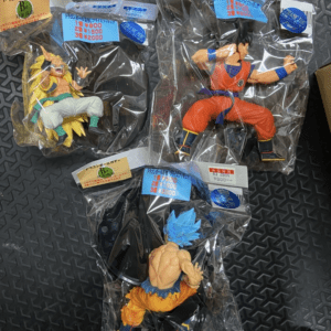 Three Dragon Ball Z action figures in sealed bags on a dark patterned floor.