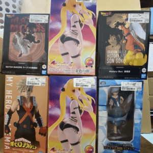 Six boxed anime figures arranged on a table, including two identical blonde female figures in swimsuits in the center boxes with other anime boxes around them (My Hero Academia on the left, Dragon Ball Z on the right).