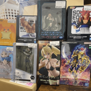 Display of assorted boxed anime and video game character figures arranged on shelves, with titles including Sword Art Online, Evangelion, and other anime/game franchises visible on the packaging.