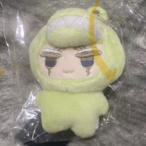 Light-green plush toy in a hooded outfit with sleepy embroidered eyes, sealed in clear packaging.