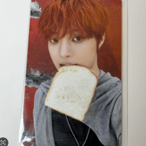 Person with bright red hair biting a slice of white bread against a red backdrop.
