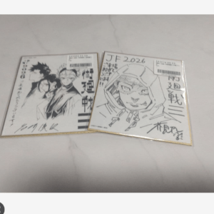 Two signed Japanese manga booklets with black‑and‑white illustrations lying on a light surface, one showing a group of characters and the other a helmeted figure.