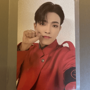 Portrait of a person with short dark hair in a red uniform, fist raised toward the camera in a selfie pose.
