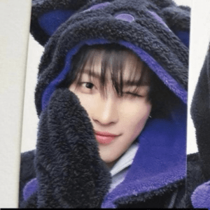 Close-up of a person in a fluffy black and purple hoodie, winking and smiling.