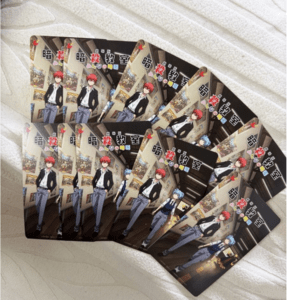 Set of manga cards spread on a white towel, showing red-haired and blue-haired characters in a hallway.
