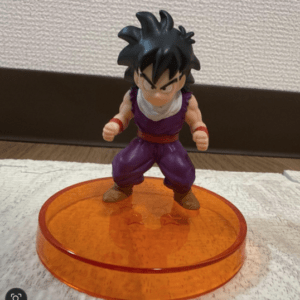 Anime action figure with spiky black hair, purple gi, white scarf, standing on an orange circular base.