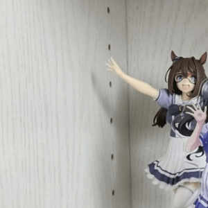 Anime character standees in a light wood cabinet; a tall figure reaches toward perforations on the back wall, with two smaller cutouts at the base.