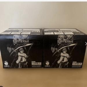 Two black Death Note figure boxes displayed side by side on a beige surface, showing illustrated characters on the front.