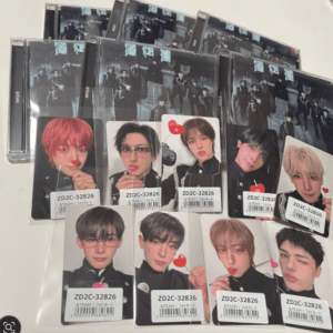Collection of glossy photo cards featuring male band members arranged on a table, with several CD cases in the background. Each card shows a solo portrait with small stickers and barcodes visible.