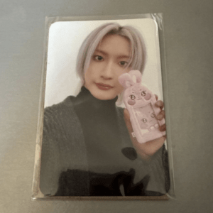 Self-portrait of a person with lavender hair in a black turtleneck and gray cardigan, holding a pink bunny-themed phone case in front of a white background.