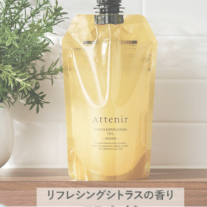 Golden Attenir Skin Clear Cleanse Oil pouch with a citrus scent, standing on a wooden counter beside a green plant.