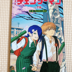 Japanese manga cover: a blue-haired girl and blond boy in school uniforms outside a campus, pink petals in the air, bold red title at top.