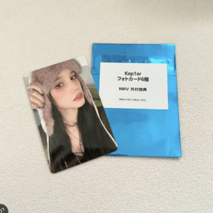 Photo card of a young woman in a pink furry hat beside a blue envelope with a white label on a light surface