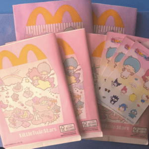 Pink Little Twin Stars packaging with yellow McDonald’s arches and cartoon sticker sheets spread on a blue surface, showing a toy/kid product set.