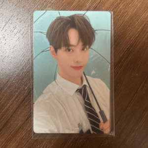 Laminated photo card showing a young man in a white shirt and striped tie, holding a clear umbrella against a teal background on a wooden table