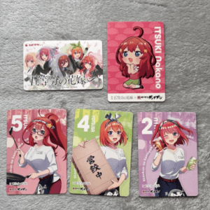 Five colorful anime trading cards laid out on a gray surface: a group image on the top-left, a single pink card on the top-right, and three character cards numbered 5, 4, and 2 on the bottom row featuring a red-haired girl in different poses and outfits.