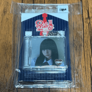 K-pop photocard featuring a young woman with long black hair, shown in clear plastic packaging on a wooden table.
